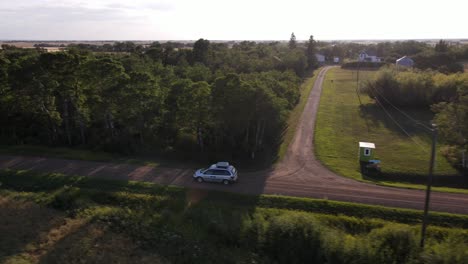 sideways following aerial shot of silver minivan driving along dusty gravel road in rural alberta