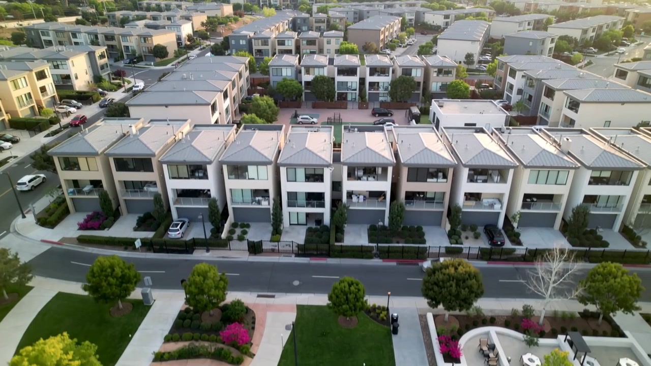 Dron volador iniciando un descenso frontal, capturando una hilera de adosados de tres plantas y una plaza verde