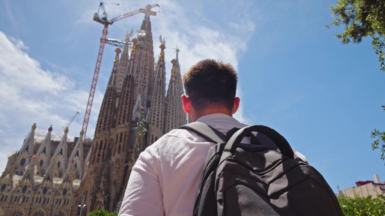 Turista con zaino che ammira la basilica della Sagrada Familia a Barcellona, Spagna, iconico capolavoro di Gaudí e celebre monumento architettonico in una soleggiata giornata estiva.