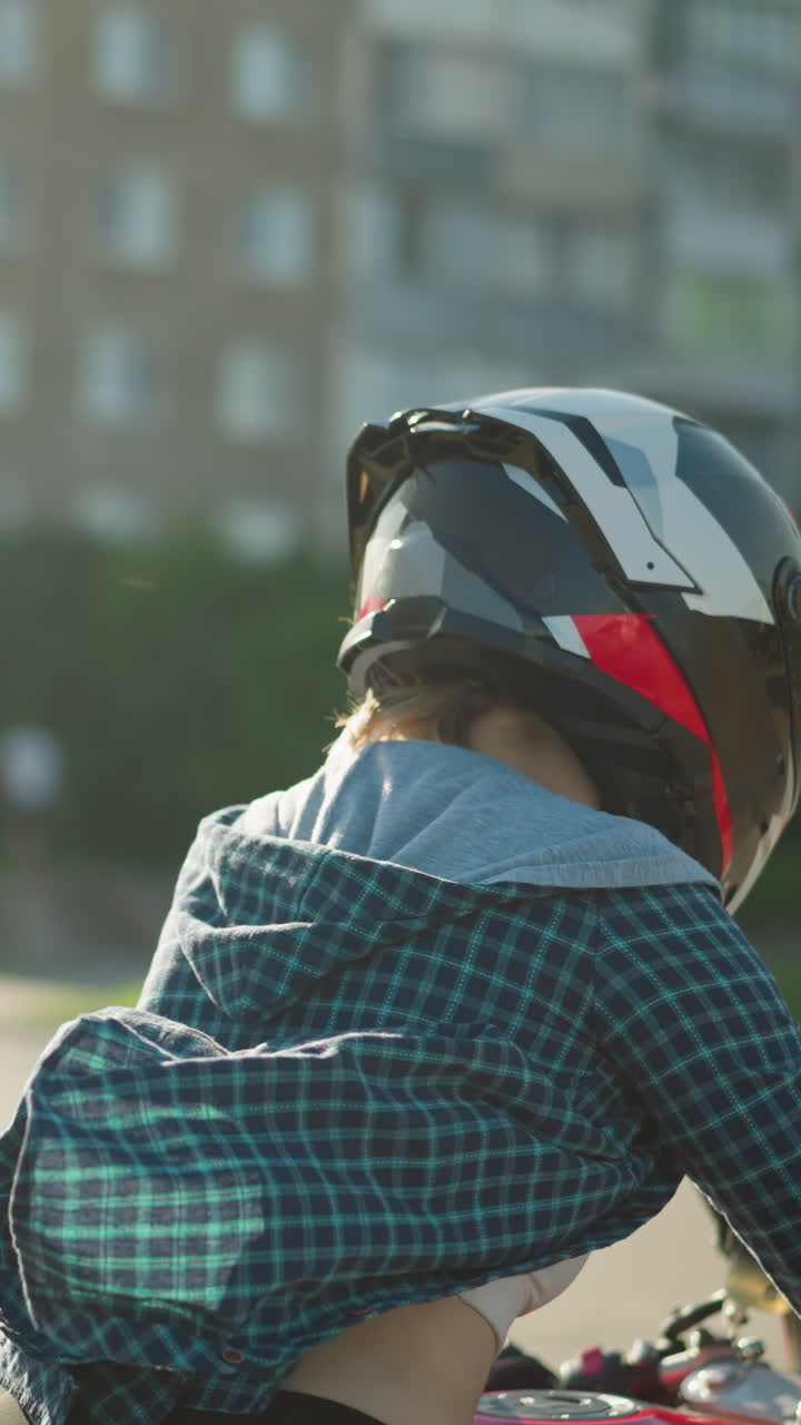 A lady rides a power bike on a sunny day with her helmet on, her checkered shirt fluttering in the wind, the sun reflects off her back as she moves through an urban environment