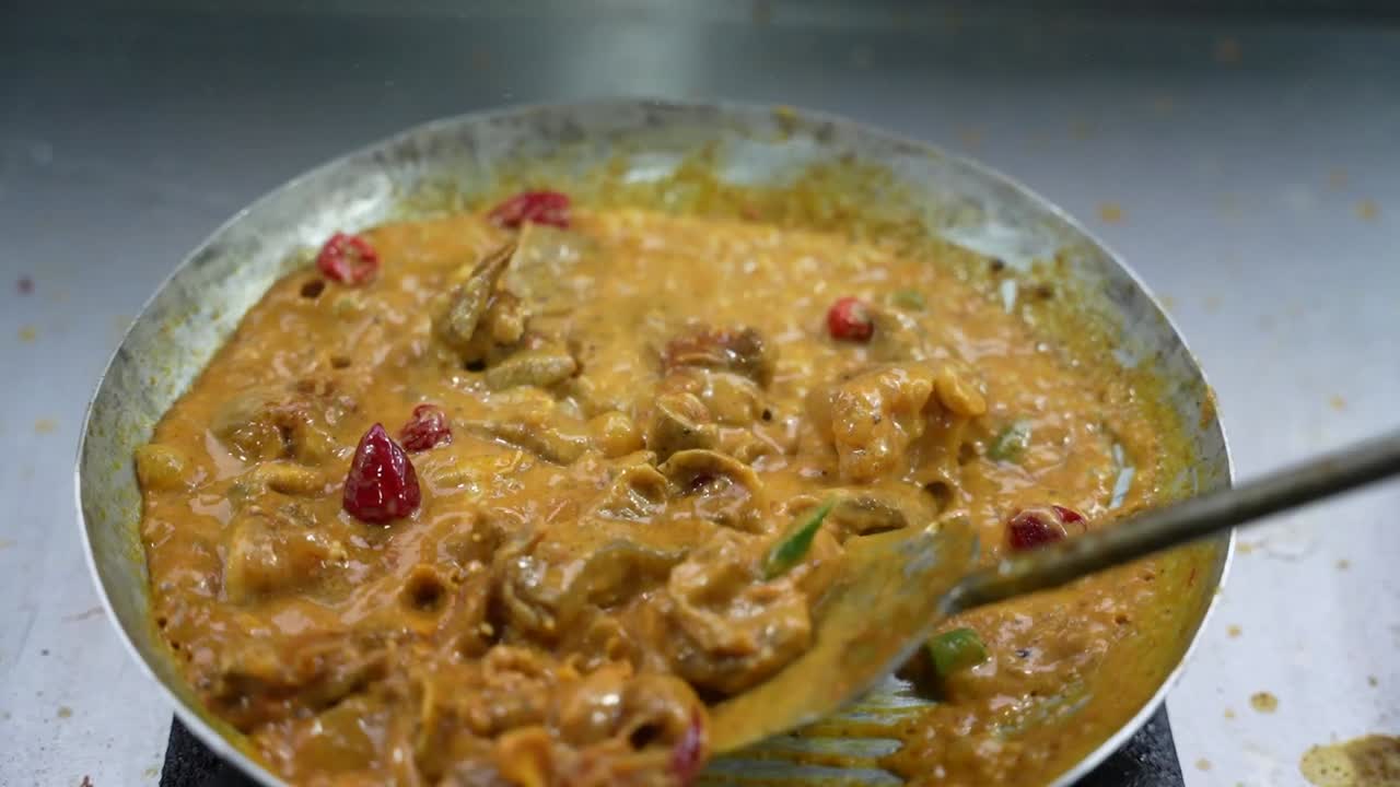 Stirring Chicken Karahi in hot spices, oil and chilies at a South Asian eatery.