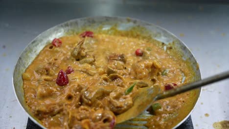 stirring chicken karahi in hot spices, oil and chilies at a south asian eatery.