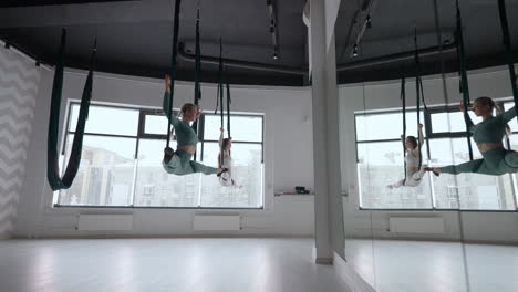 the interior shooting of an two women practices different inversion antigravity yoga with a hammock in yoga studio. the balance between mental and physical two person effort and achievement concept