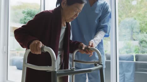 smiling asian female doctor helping senior female patient to walk using walking frame