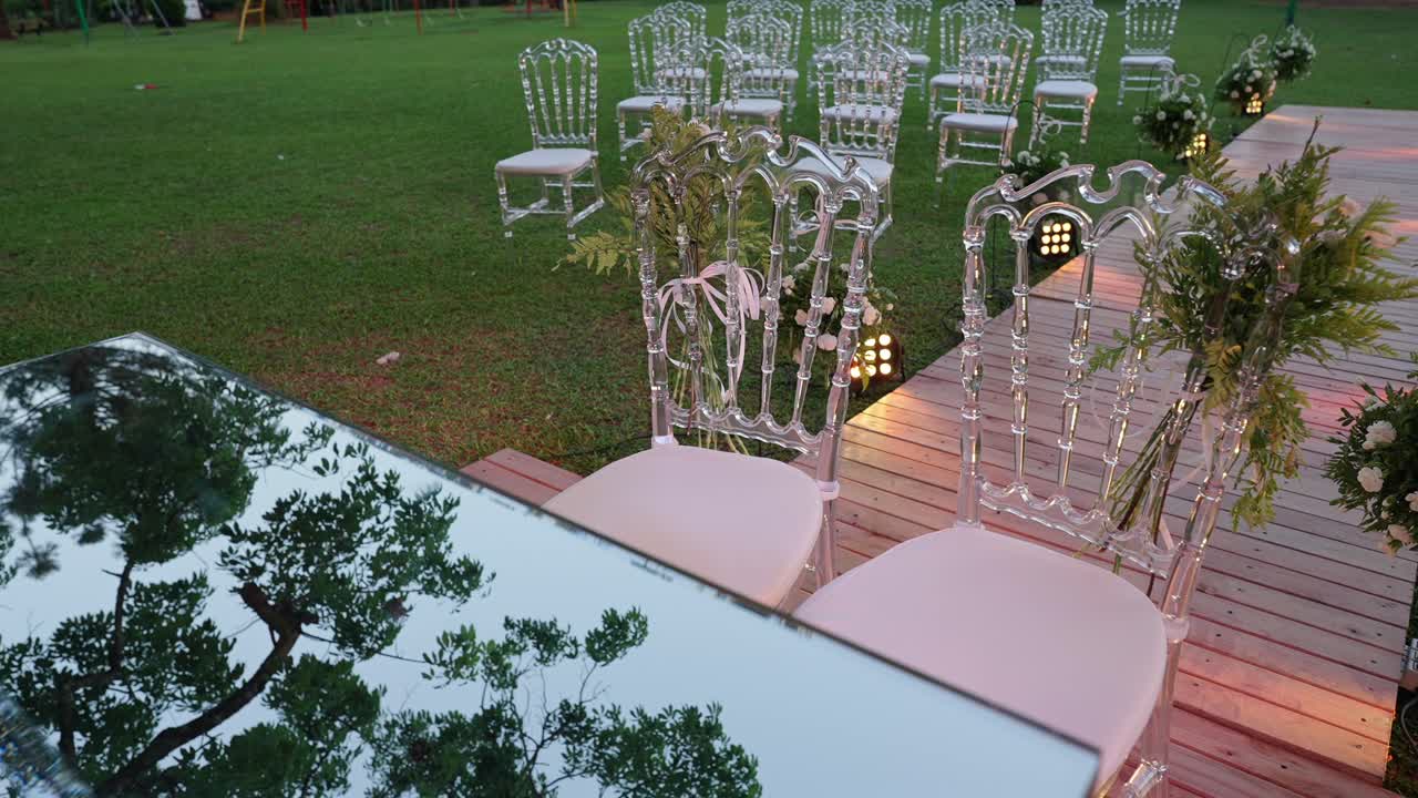 Allestimento per cerimonia di matrimonio all'aperto con corridoio decorato, composizioni floreali ed eleganti sedie trasparenti.