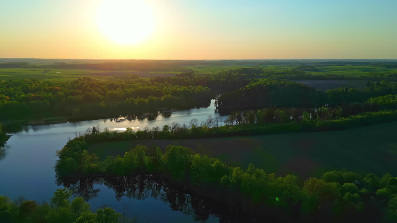 Aerial drone shot over lush green vegetation around the winding river with sun rising in the background