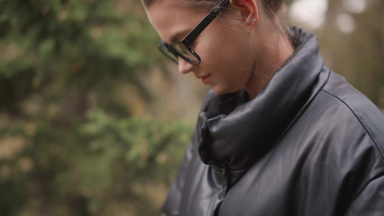 Close up of young woman wearing glasses and black puffer jacket holding bread in her hands. subject examines food item with soft natural light illuminating details like painted nails