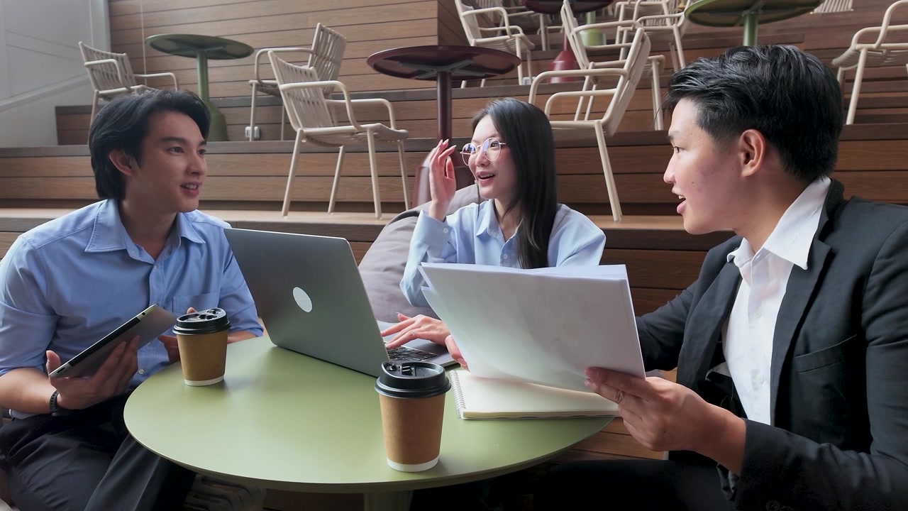 เพื่อนร่วมงานชาวเอเชียหลากหลายเชื้อชาติกำลังร่วมมือกันทำงานเอกสารและแท็บเล็ตดิจิทัลในบรรยากาศสำนักงานที่สว่างสดใสในกรุงเทพฯ