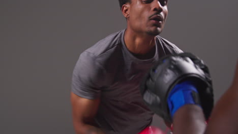 Studio-Shot-Of-Male-Boxer-Sparring-Working-Out-With-Trainer-Wearing-Punch-Mitts-Or-Gloves-Practising-For-Fight-11