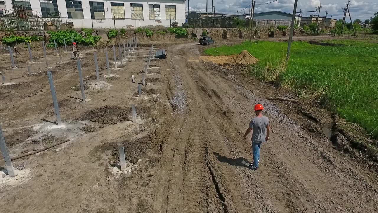 Engineer in orange helmet walks. Technical expert is walking to the construction of a new solar power plant on the field. Top view.