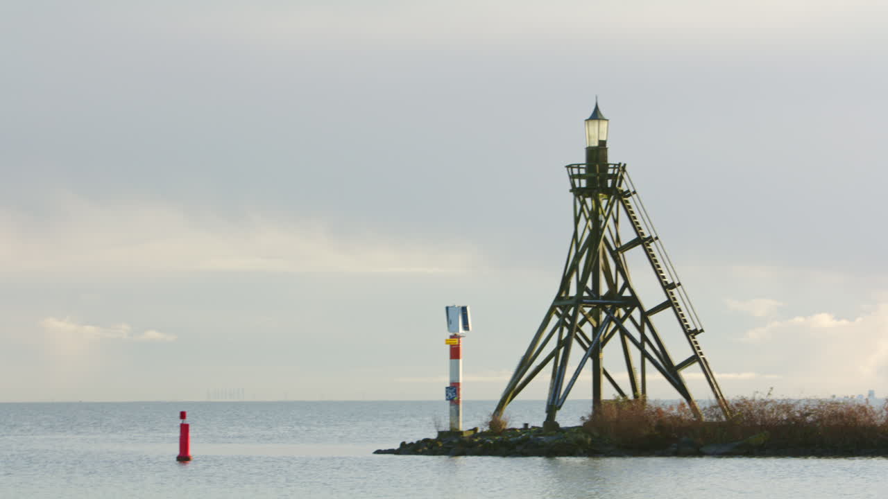 Minimalistisk maritim scene som viser et navigasjonsfyr i tre som står ved strandlinjen med rolig sjø og myk himmel, ideelt for konsepter som navigasjon, sikkerhet, retning og kystinfrastruktur