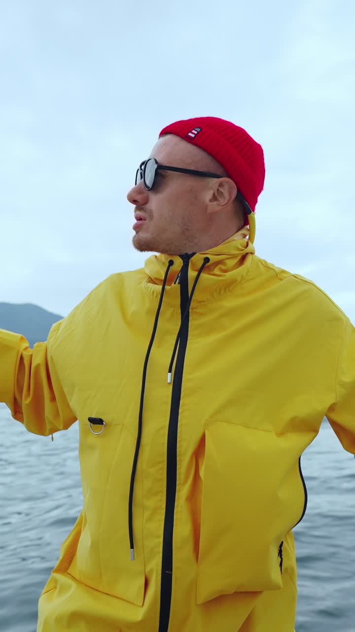 Abenteuerlustiger Mann in gelbem Regenmantel und roter Mütze auf einem Boot