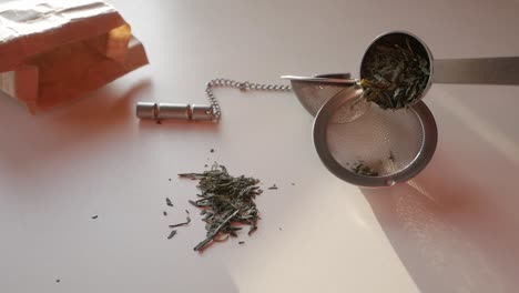 fresh green tea leaves being prepared for brewing with a tea infuser and a paper bag