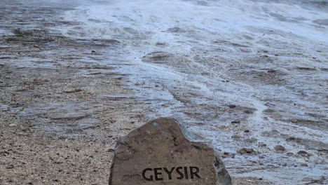 geysir sign on rock and vapor above geyser in geothermal area of iceland