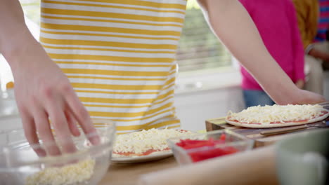 Diverse-group-of-teenage-friends-cooking-and-making-pizza-in-kitchen,-slow-motion