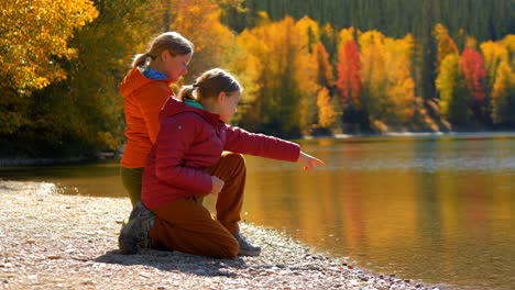 two girls by a lake with vibrant autumn trees