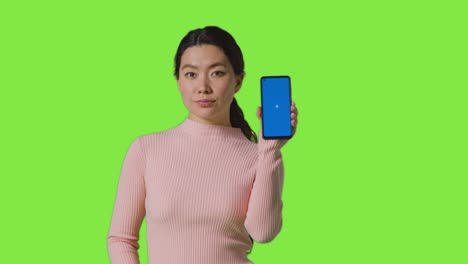 Studioporträt-Einer-Frau,-Die-Ein-Bluescreen-Handy-In-Richtung-Kamera-Vor-Einem-Greenscreen-Hält