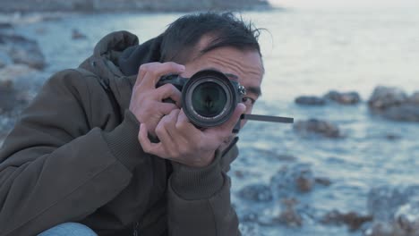 young nepali man looking through camera viewfinder at rocky coastline