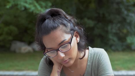 Retrato-De-Una-Chica-Guapa-Con-Gafas-Que-Se-Siente-Triste-Al-Aire-Libre-En-El-Parque,-Pone-La-Cabeza-En-La-Mano-Con-Decepción-Mostrando-Emociones