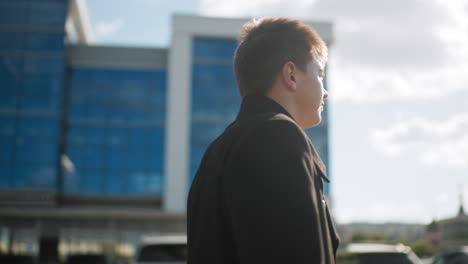 man in black coat walking confidently during sunny day, sun reflecting off him, with glass building in urban background, symbolizing professionalism and modern business lifestyle