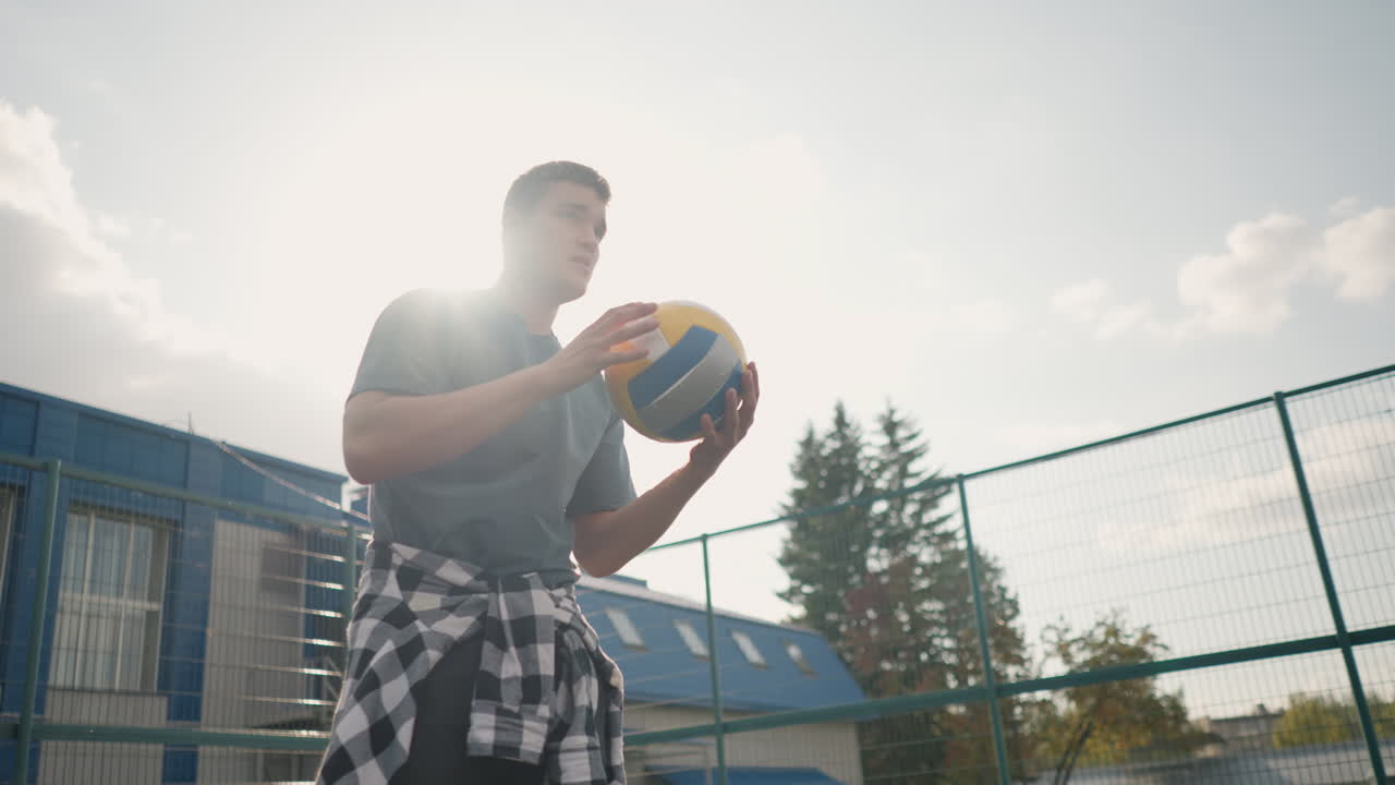 훈련 중에 배구공이 배구공을 돌리는 선수, 배경에 초록색과 건물이 있는 스포츠 경기장에서 야외에서 찍은 사진