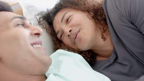 pareja de hombres homosexuales felices y diversos acostados en la cama sonriendo y hablando en casa, en cámara lenta