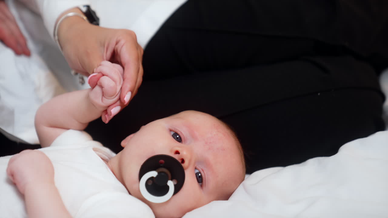 Lovely newborn with a pacifier in mouth. Mom holds a tiny baby hand. Close up.