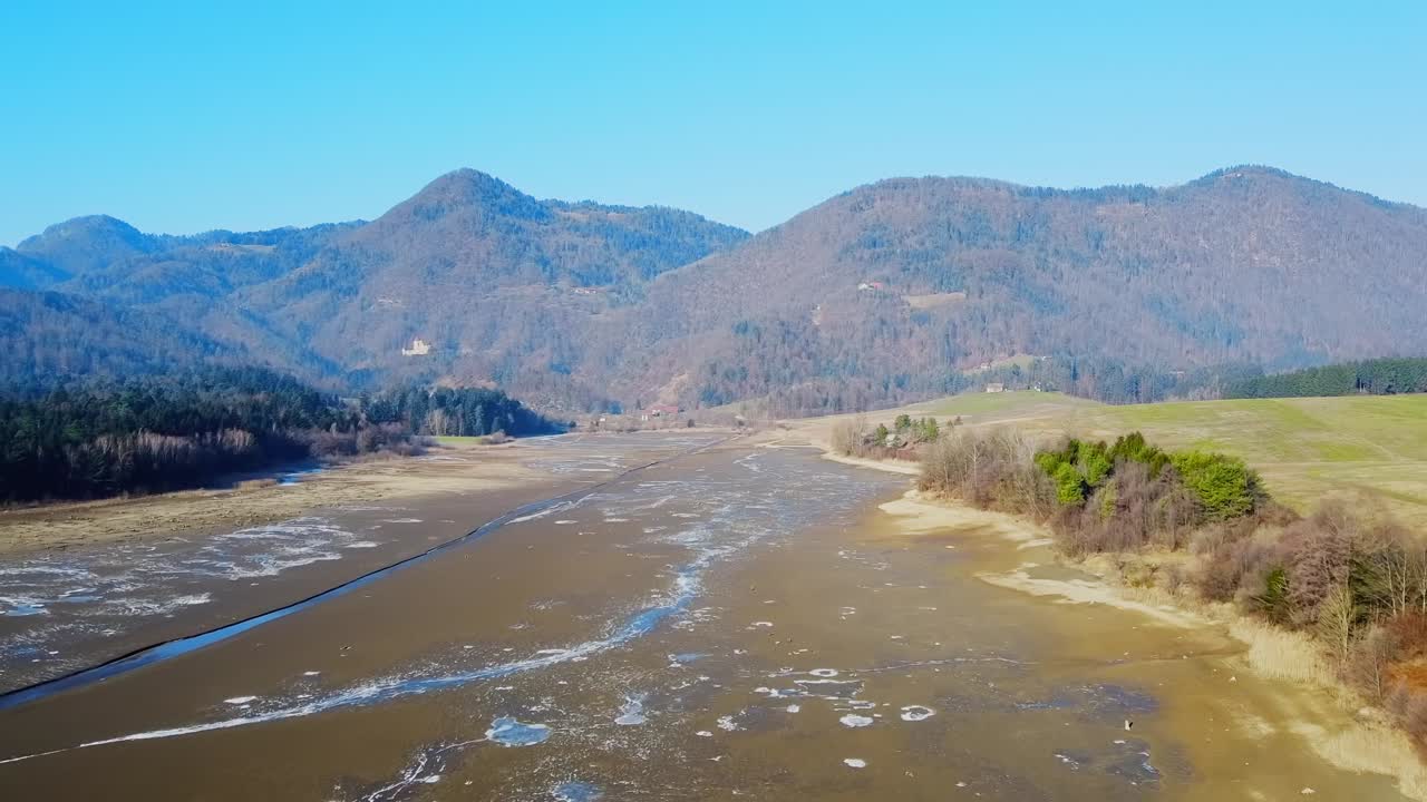 Aerial over the dried lake with cracks and crevices filled with scanty water amidst beautiful valley of green mountains