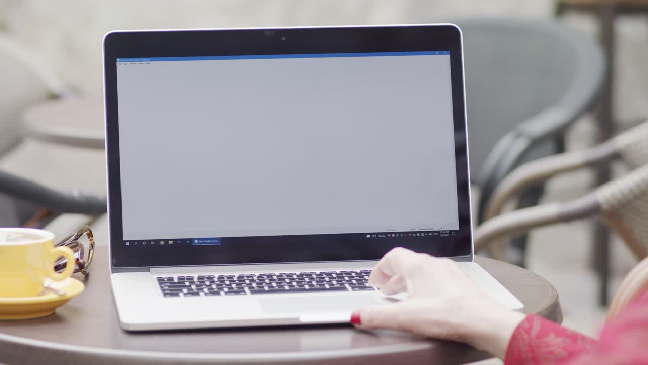 Over-the-shoulder shot of a woman working on a laptop at an outdoor cafe. The screen is blank, perfect for adding your own website, application, or video content.