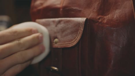 hand polishing flap of a brown leather bag with wax - close up