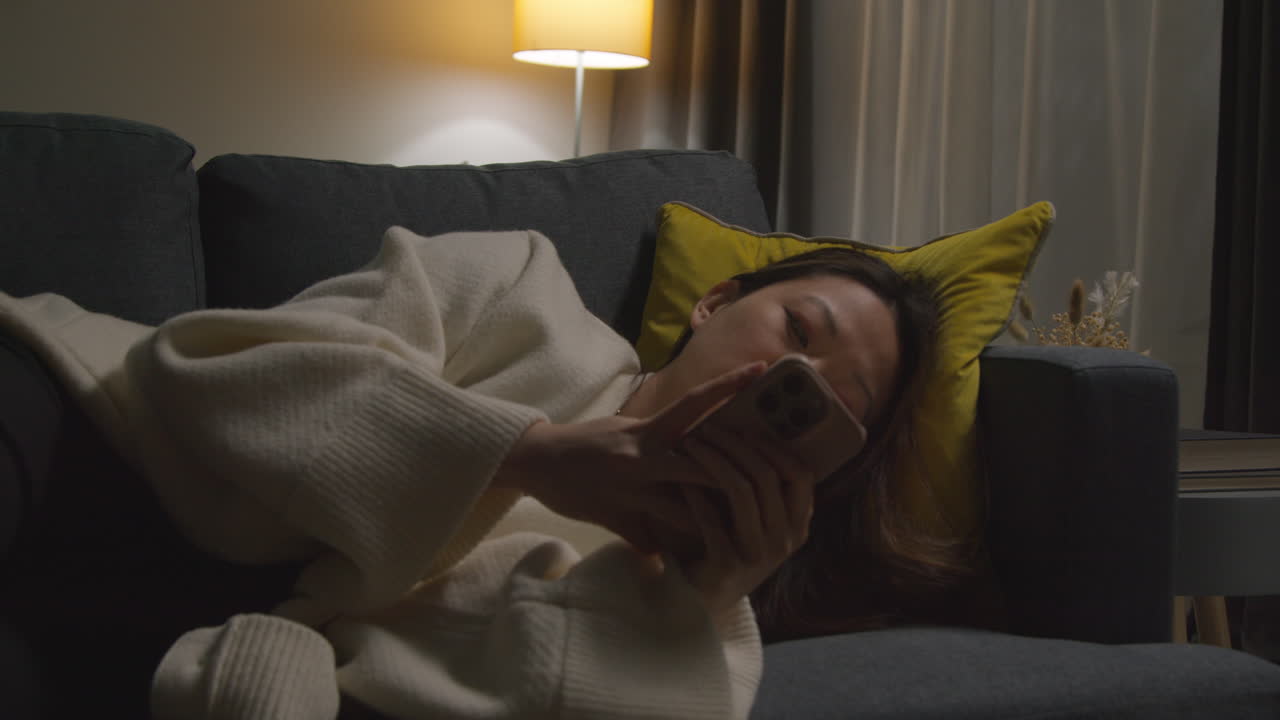 집에서 저녁을 보내고 소파에 누워 휴대전화를 들고 인터넷이나 소셜 미디어를 스크롤하는 여성 6