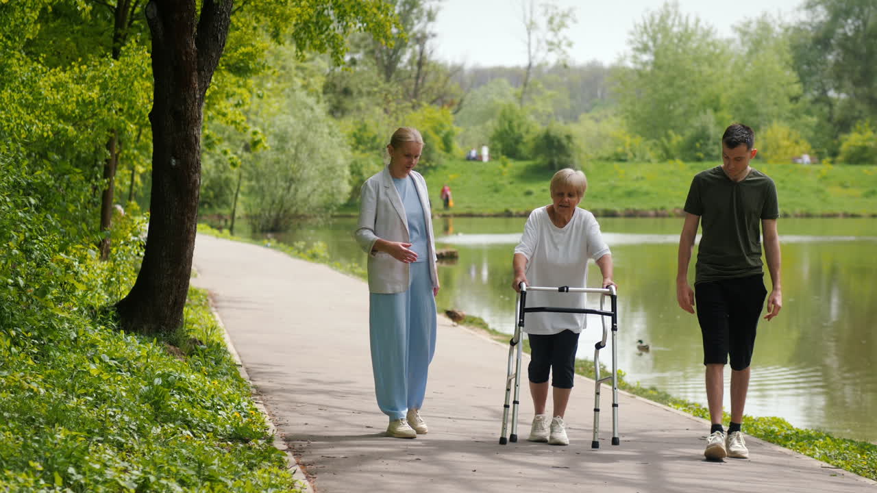 Elderly Woman with Walker Assisted by a Nurse and Young Man in a Park