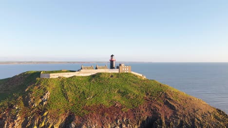 a lone lighthouse sits on a lush green cliff by the sea in ballycotton, county cork, ireland