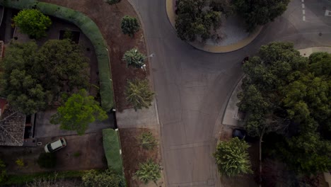 Vista-Aérea-De-Arriba-Hacia-Abajo-De-Un-Automovilista-Haciendo-Un-Círculo-De-Tráfico-En-Una-Calle-Residencial-Tranquila-Al-Lado-De-Una-Presa