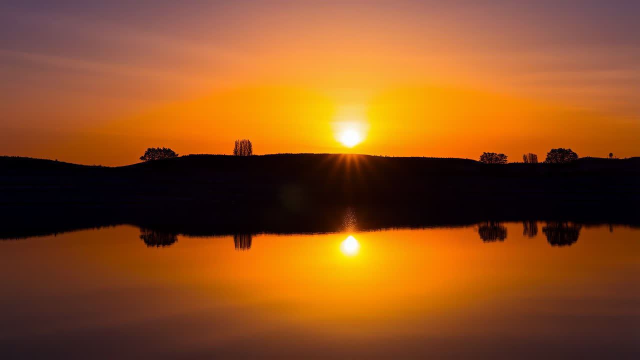 Vibrant Sunset Reflection over Water with Silhouetted Trees