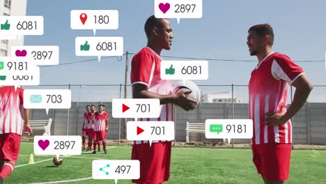 social media icons over two diverse male soccer players talking to each other on sports field