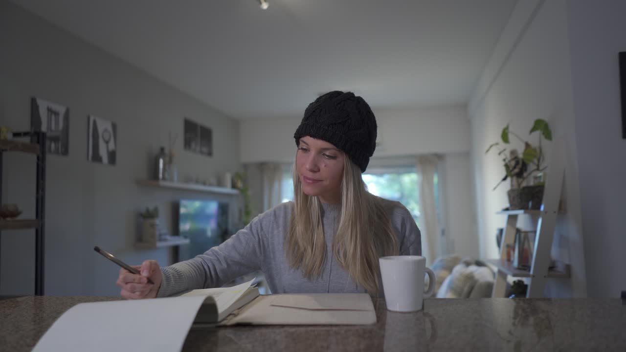 A beautiful blonde woman writing on a notebook and drinking a hot beverage at home