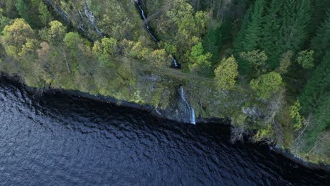 Water-stream-passing-below-wid-narrow-countryside-road-at-autumn,-aerial-Norway