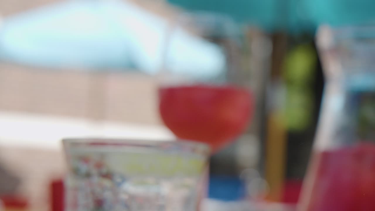 Hand pours red cocktail into wine glass outdoors in daylight, with shallow depth of field