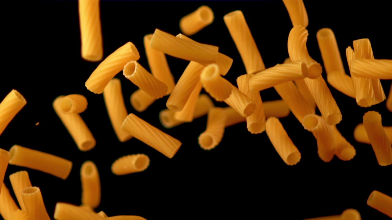 Tubetti di pasta maccheroni secchi che cadono al rallentatore su sfondo nero