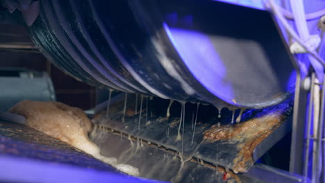 Apple juice dripping from the rotating shaft. Machine squeezing fruit at automated line of food factory. Close up.