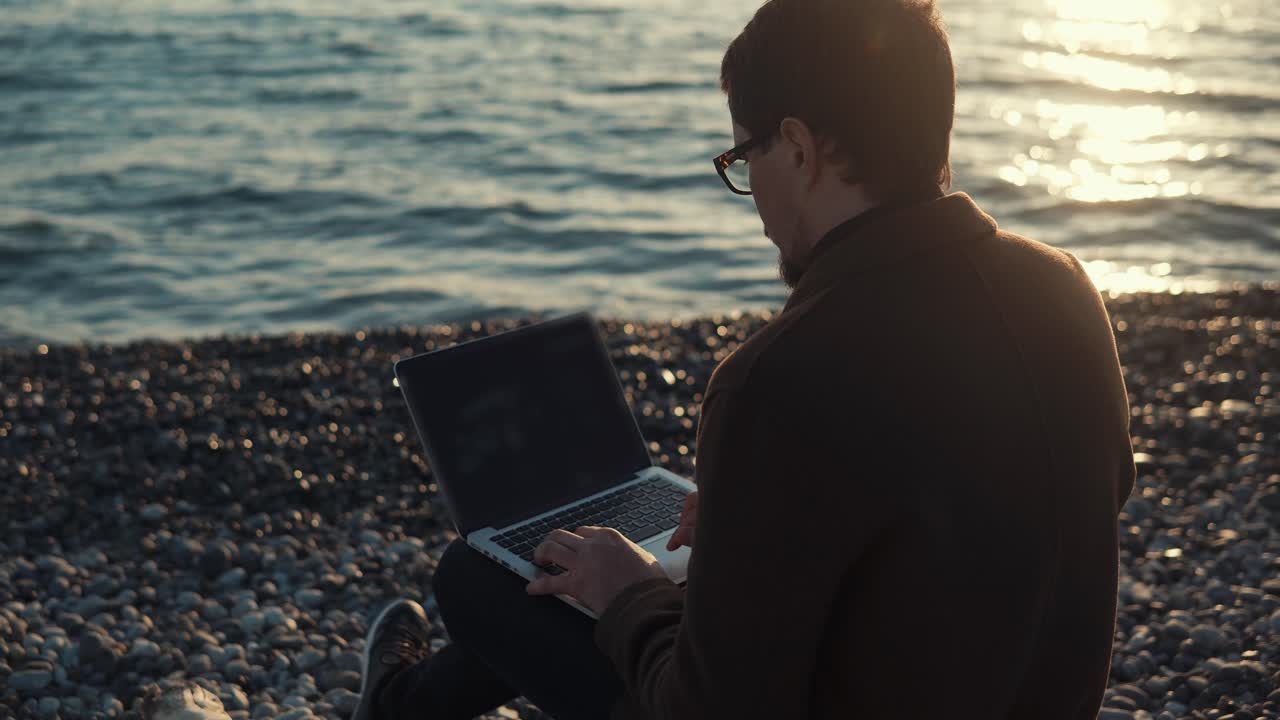 hombre trabajando en una computadora portátil en la playa al atardecer