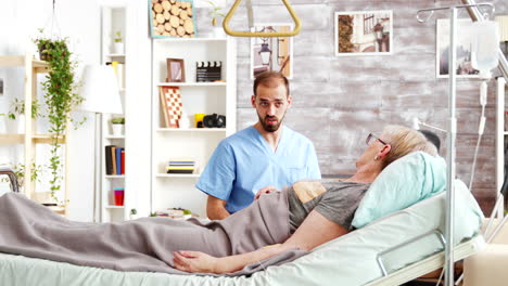 médico masculino teniendo una conversación con una anciana enferma acostada en una cama de hospital en un hogar de ancianos
