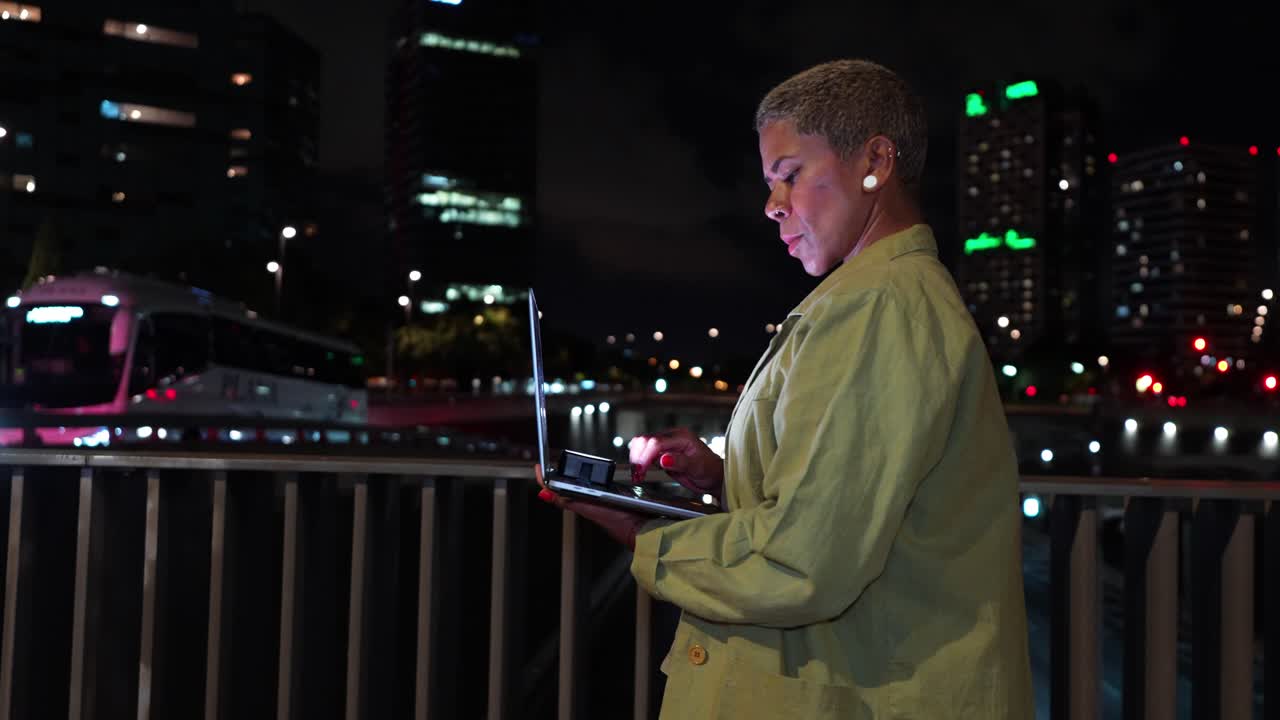 Woman Interacting with Laptop Screen on City Bridge at Night