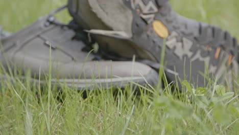 Dolly-closing-in-to-worn-hiking-boots-in-a-field-of-grass-on-a-sunny-day