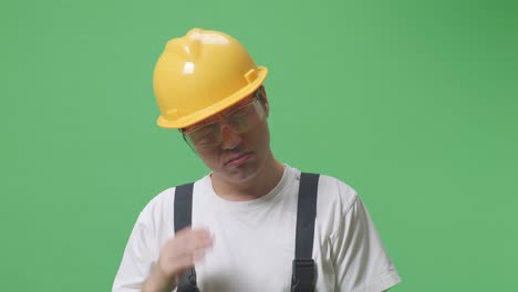 close up of asian man worker wearing goggles and safety helmet having a headache while standing in the green screen background studio