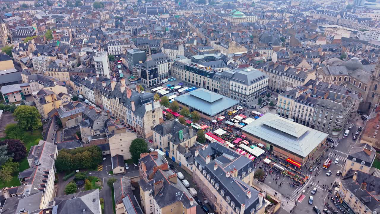 Drone pans laterally over Place des Lices in Rennes during market day with colorful stalls and crowds