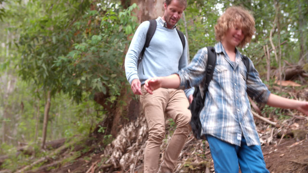 아버지와 아들은 카메라를 향해 숲에서 언덕 아래로 고 있습니다.