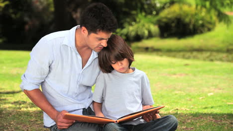 Padre-E-Hijo-Sentados-Leyendo-Al-Aire-Libre