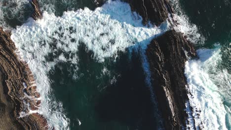 Drone-shot-of-waves-washing-over-sharp-rocky-cliffs